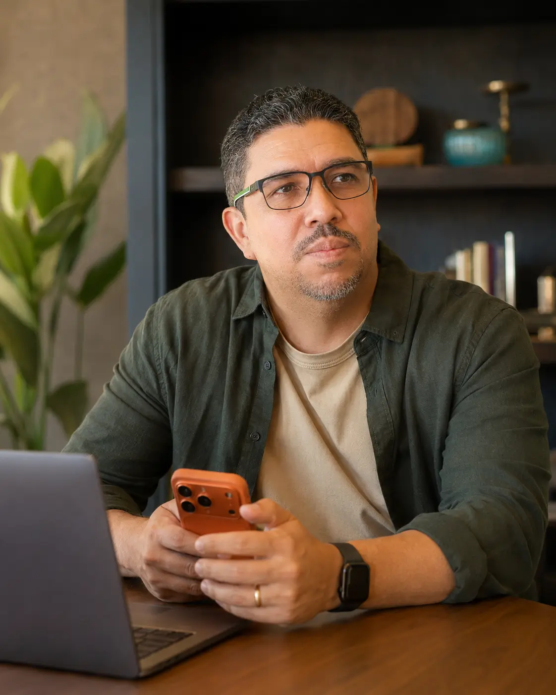 Isaac Andrade em ambiente de trabalho, sentado à mesa com um smartphone laranja e um notebook